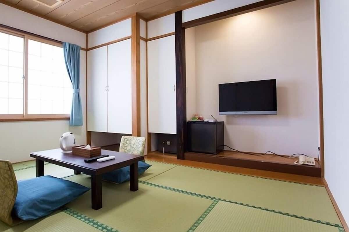 Une pièce de style japonais traditionnel, avec un sol recouvert de tatamis, une table basse, un canapé, un téléviseur et un meuble.