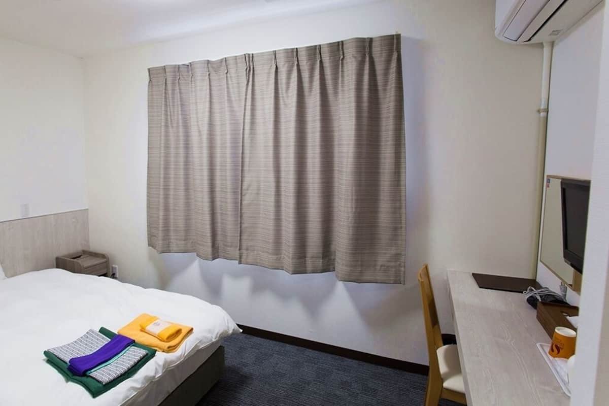 Une chambre d’hôtel équipée d’un lit, d’un bureau, d’une chaise, d’une table de chevet, d’une fenêtre avec des rideaux et d’un appareil de climatisation.