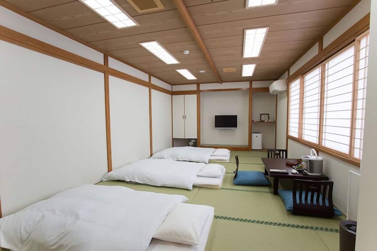 Une pièce de style japonais traditionnel, avec un sol recouvert de tatamis, un futon servant de lit, une télévision et un bureau avec une chaise.