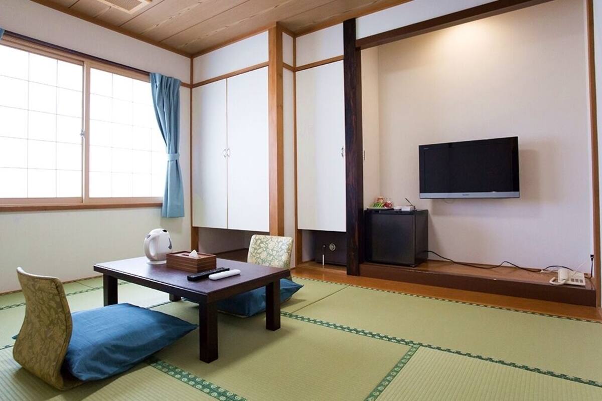 Une pièce de style japonais traditionnel, avec un sol recouvert de tatamis, une table basse avec des coussins, un téléviseur et des portes coulissantes.