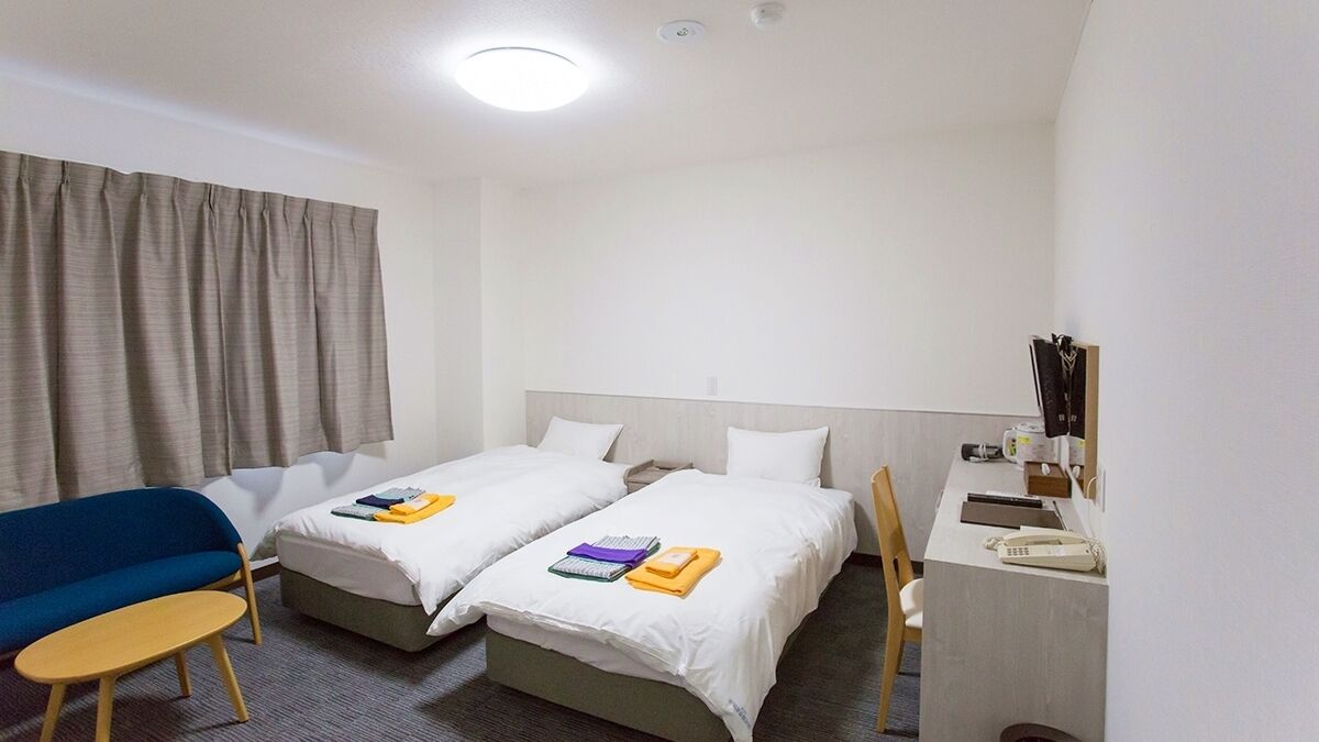 Een hotelkamer met twee bedden, een bureau, een stoel, een tafeltje en een raam met gordijnen.