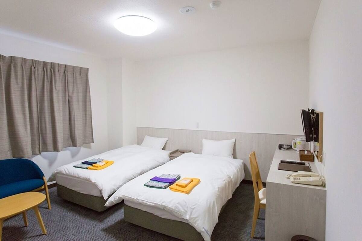 Une chambre d’hôtel avec deux lits, un bureau, une chaise, une petite table et une fenêtre avec des rideaux.