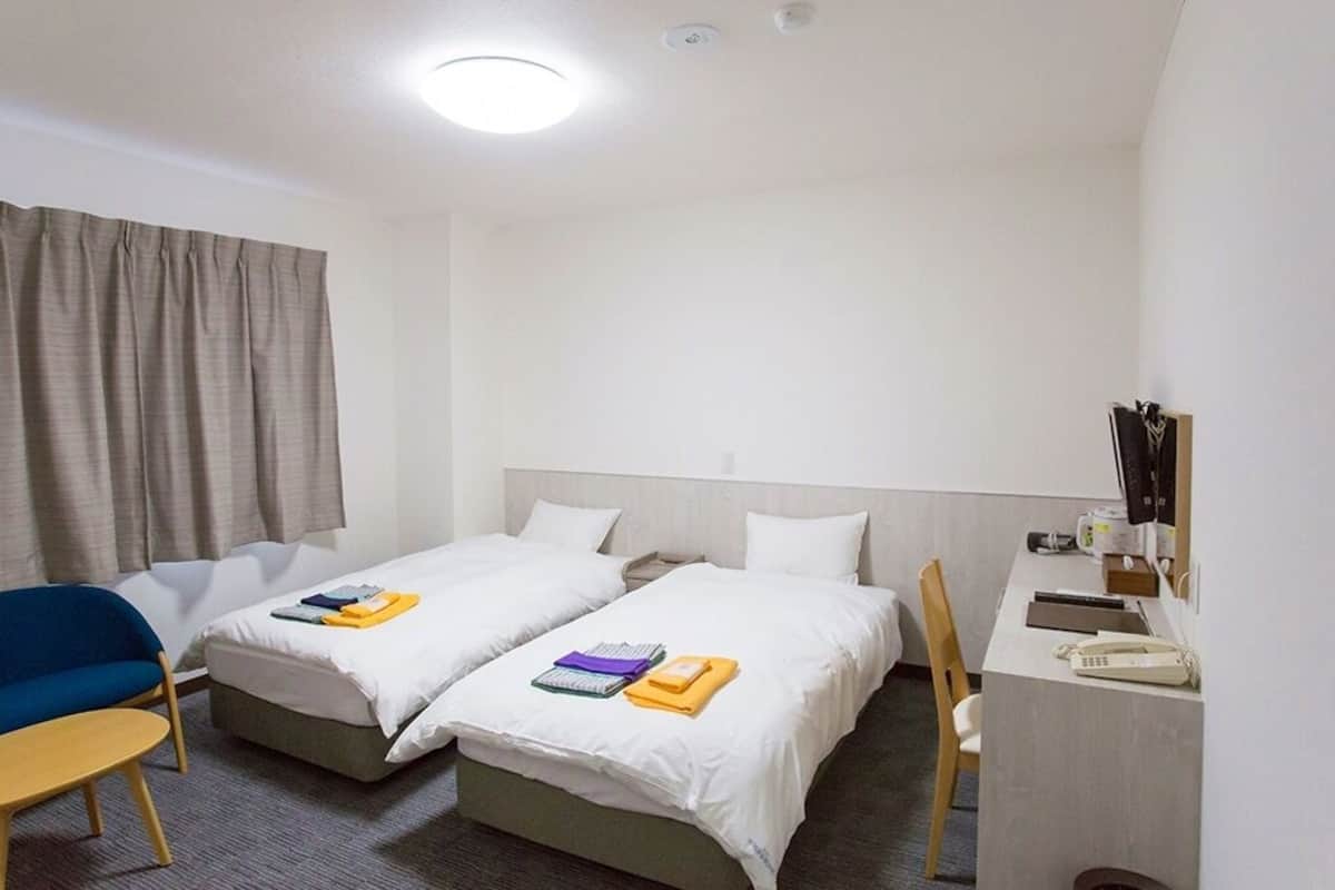 Une chambre d’hôtel avec deux lits, un bureau, une chaise, une petite table et une fenêtre avec des rideaux.