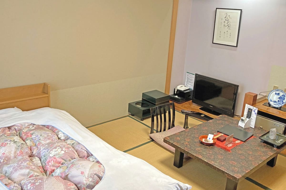 A hotel room with a bed, a television, a small table, and a chair.