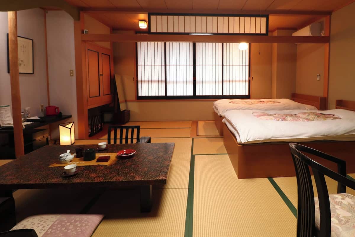 A traditional Japanese room with tatami flooring, a low bed, a wooden table with tea set, and sliding doors.
