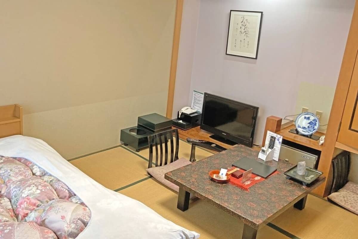 Une chambre d’hôtel avec un lit, un bureau, une télévision et une petite table sur laquelle se trouve un vase.