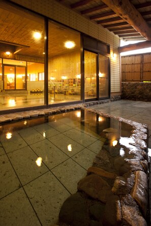 Un onsen japonais traditionnel, avec un bain en pierre, des poutres en bois et un sol carrelé.