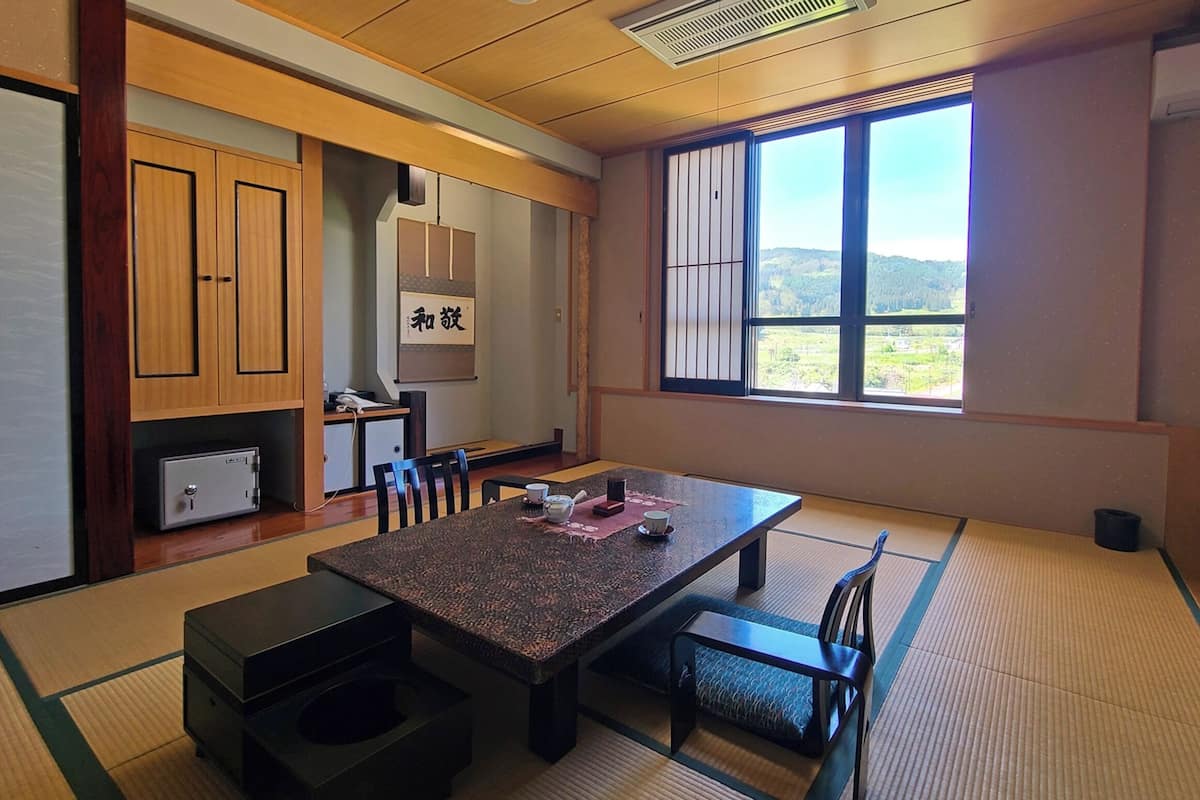 A traditional Japanese room with tatami flooring, a low table with a tea set, a sliding door, and a view of a mountainous landscape.