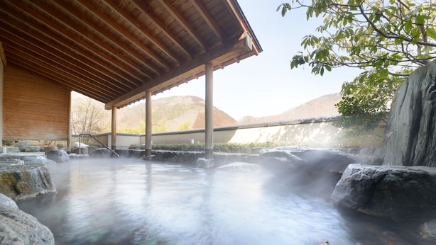 A hot spring area with a wooden structure, rocks, and a view of hills. - Surikamitei Ohtori (Fukushima)