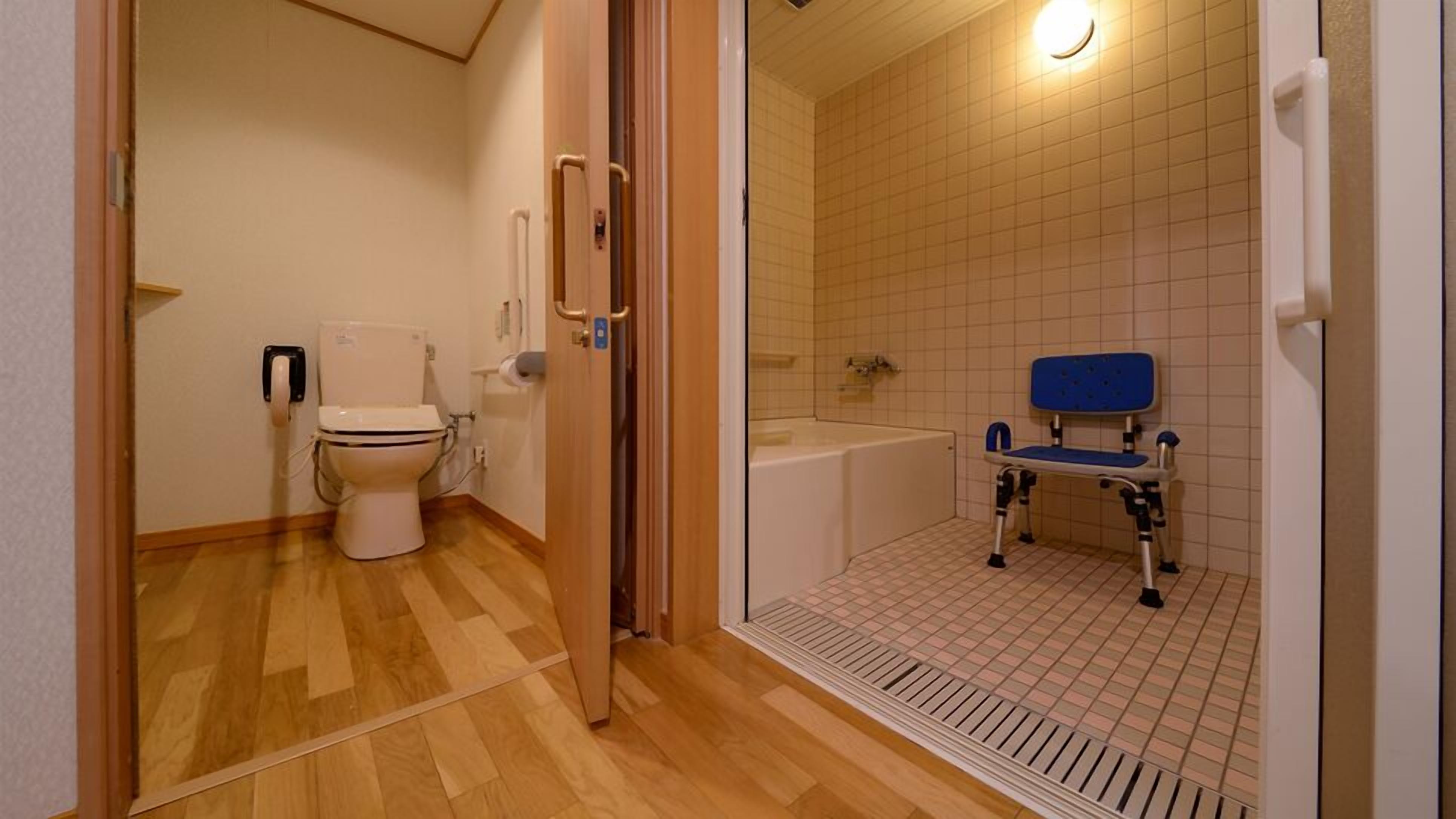 A bathroom with a toilet, a shower with a blue chair, and a bathtub.