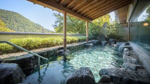 A stone hot spring with a wooden pergola overhead, surrounded by rocks and greenery. - Surikamitei Ohtori (Fukushima)