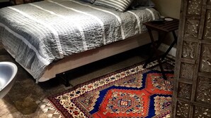 Une chambre à coucher avec un lit, une table de chevet, une lampe, une chaise et un tapis à motifs.