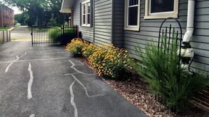 Une maison d’habitation avec une allée fermée par un portail, un chemin menant à l’entrée et un petit jardin agrémenté de fleurs jaunes et d’arbustes verts.