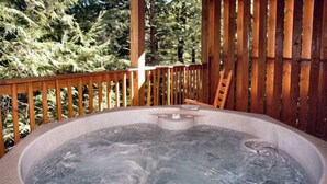 A hot tub surrounded by a wooden deck with a view of trees.