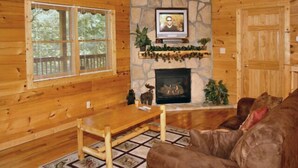 A cozy cabin interior with a stone fireplace, wooden walls, a television mounted above it, and a comfortable seating area with a couch and a coffee table.