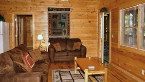 A wooden cabin interior with a brown sofa, a wooden table, and a patterned rug.