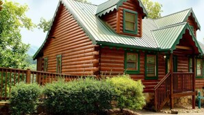 A log cabin with a steeply pitched roof, a front porch, and a stone foundation.