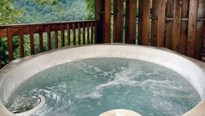 A hot tub with a wooden deck and a view of a forested landscape.