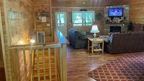 A cozy cabin interior with a wooden interior, a fireplace, a television, and a seating area with a patterned rug.