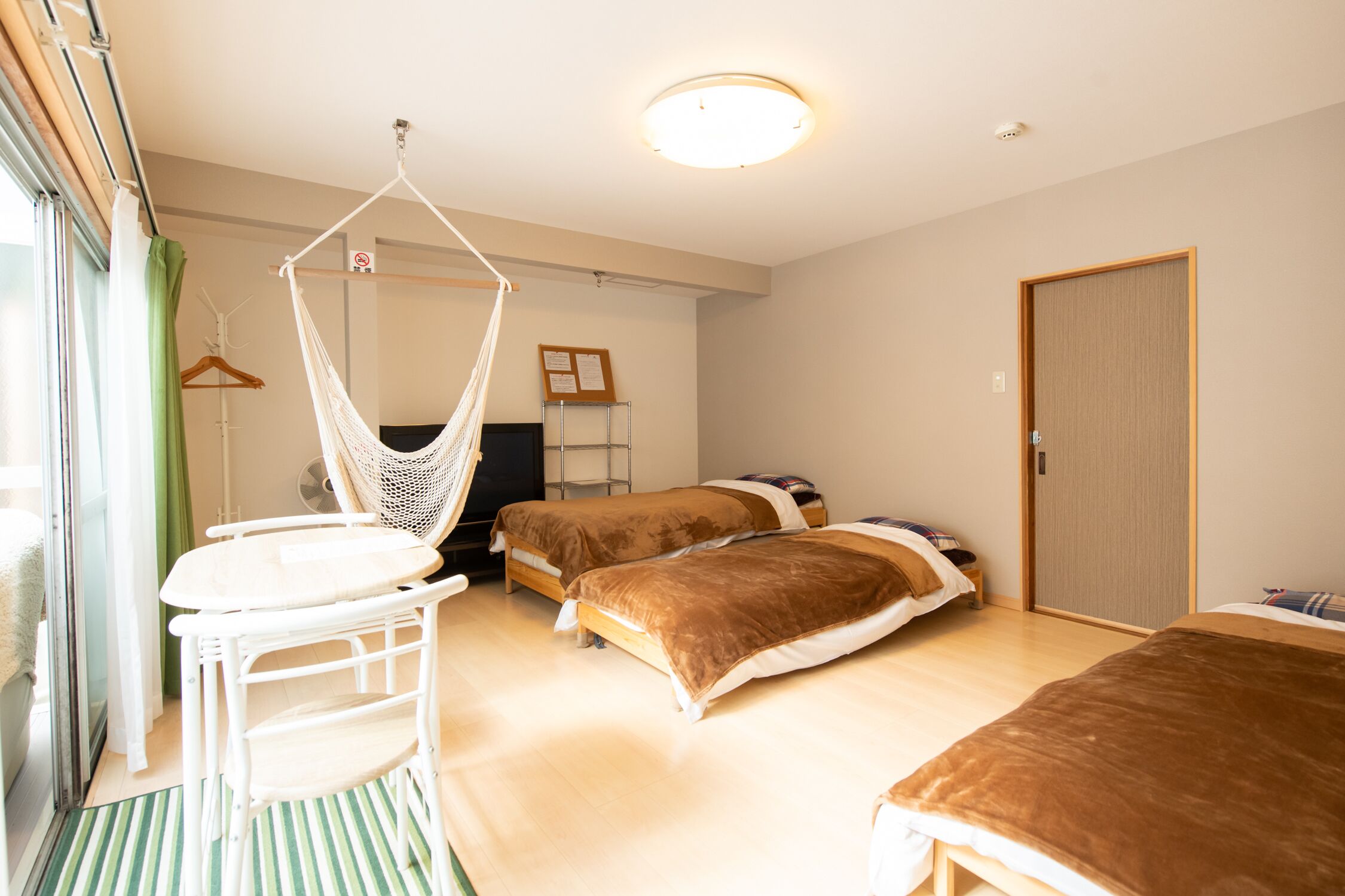 A room with two beds, a hanging chair, a small table, and a door.