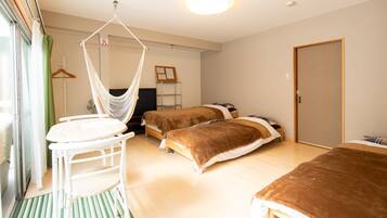 A room with two beds, a hanging chair, a small table, and a door.