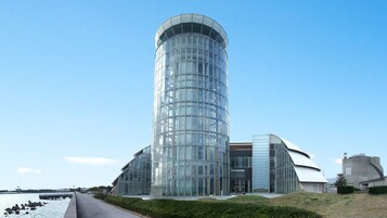 Un moderno edificio cilíndrico de vidrio con techo curvo, junto a una estructura más pequeña con techo plano.