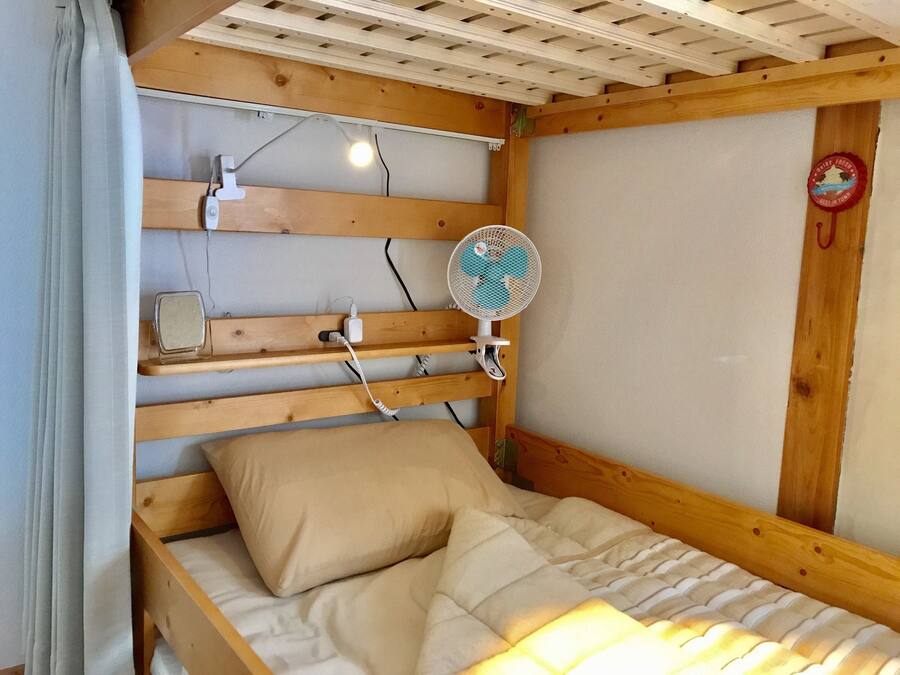 A wooden bunk bed with a headboard, a bedside table, a fan, and a wall-mounted clock.