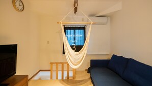 A room with a hammock chair, a blue sofa, a wooden TV stand, and a wall clock. - Destiny Inn Sakaiminato (Sakaiminato)