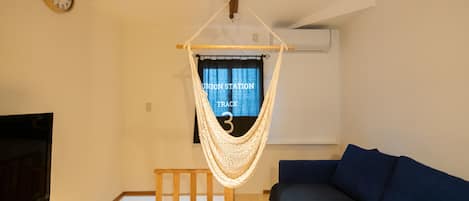 A room with a hammock chair, a blue sofa, a wooden TV stand, and a wall clock.