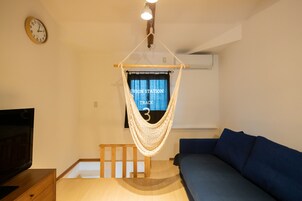 Una habitación con una silla hamaca, un sofá azul, un mueble de televisión de madera y un reloj de pared.