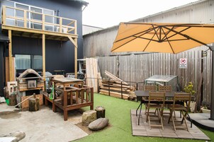 Un patio trasero con una terraza de madera, una parrilla y una mesa de comedor con sillas.