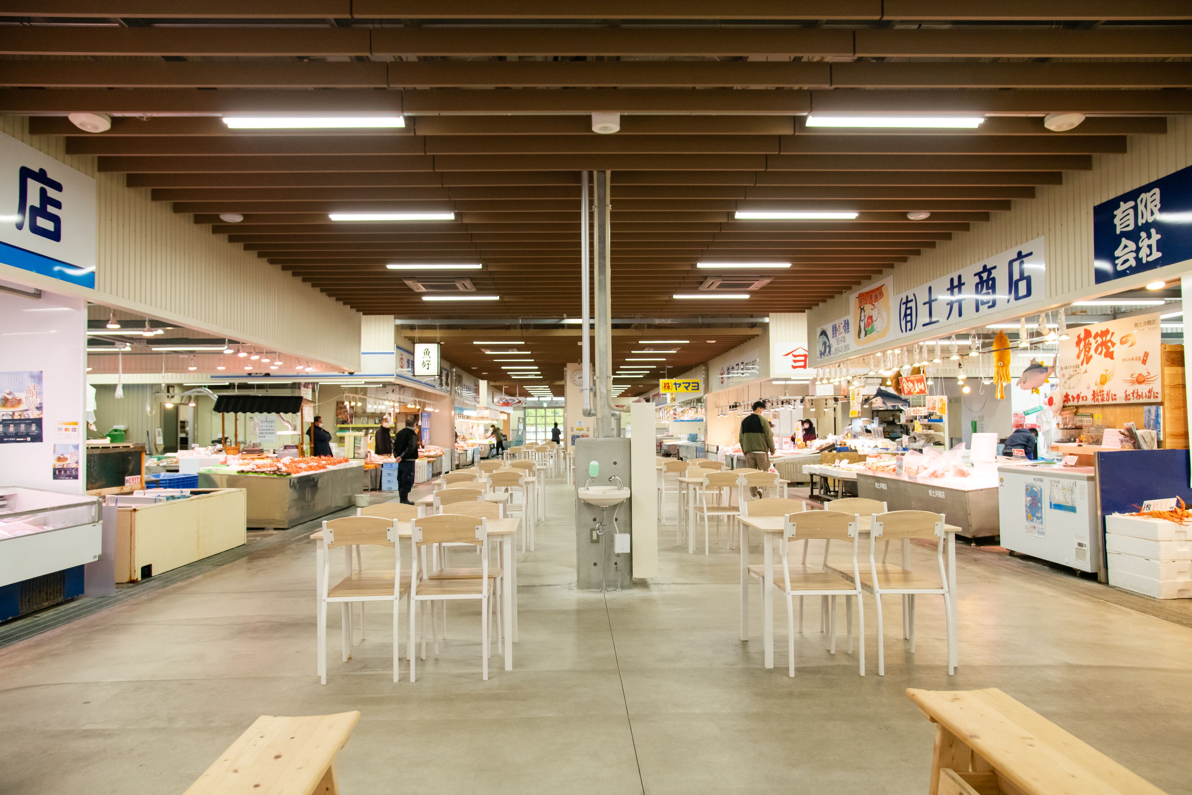 An indoor market with multiple food stalls, wooden benches, and a central sink.