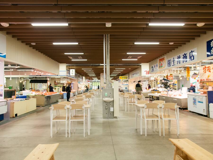 An indoor market with multiple food stalls, wooden benches, and a central sink.