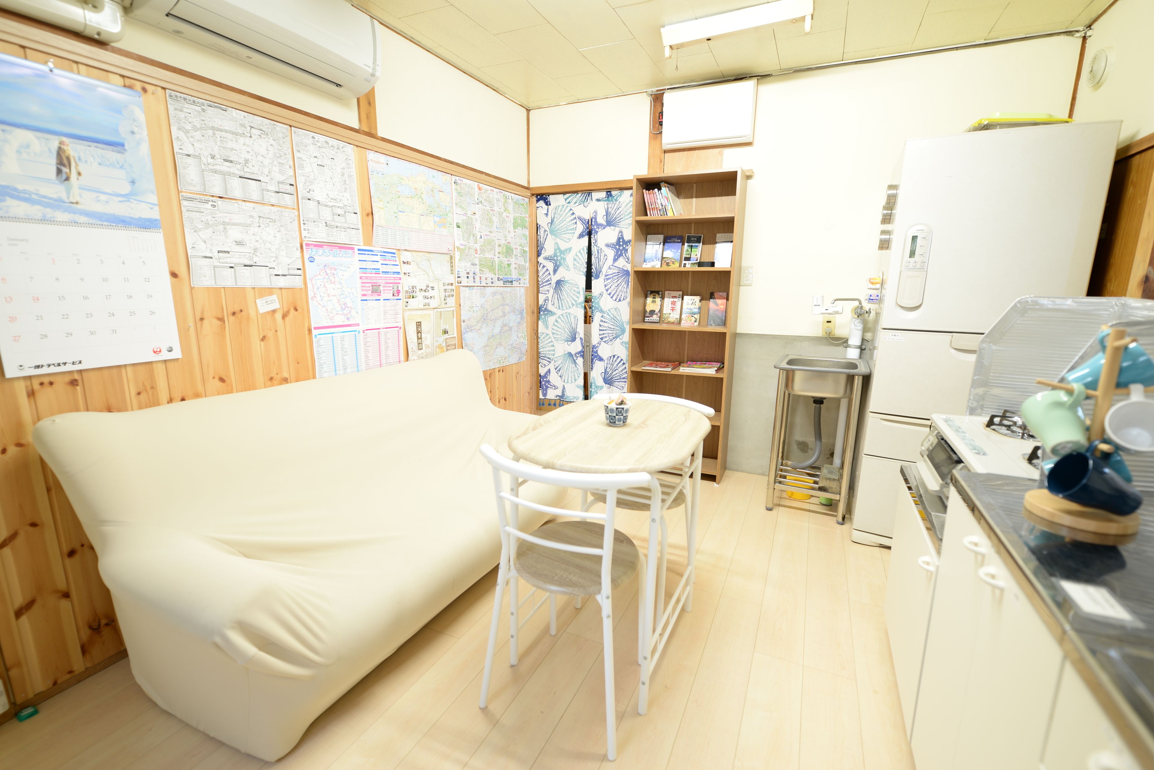 Une petite pièce agréable, avec un canapé, une petite table, une bibliothèque et un réfrigérateur.