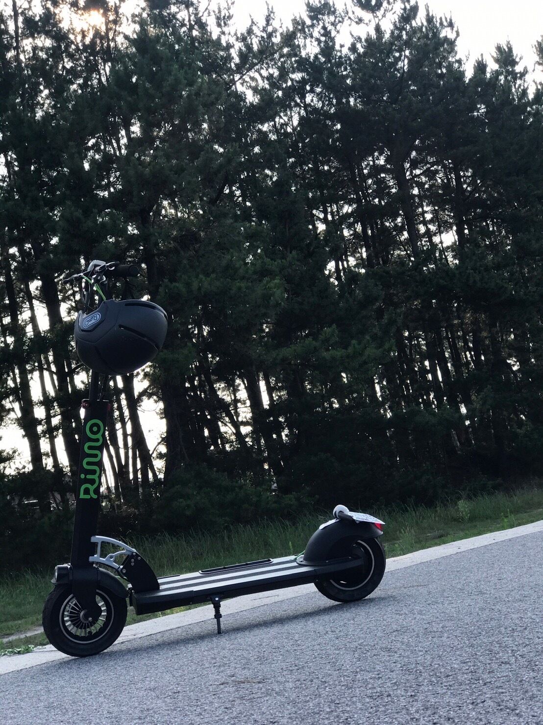 A black electric scooter parked on a road with a forest in the background.