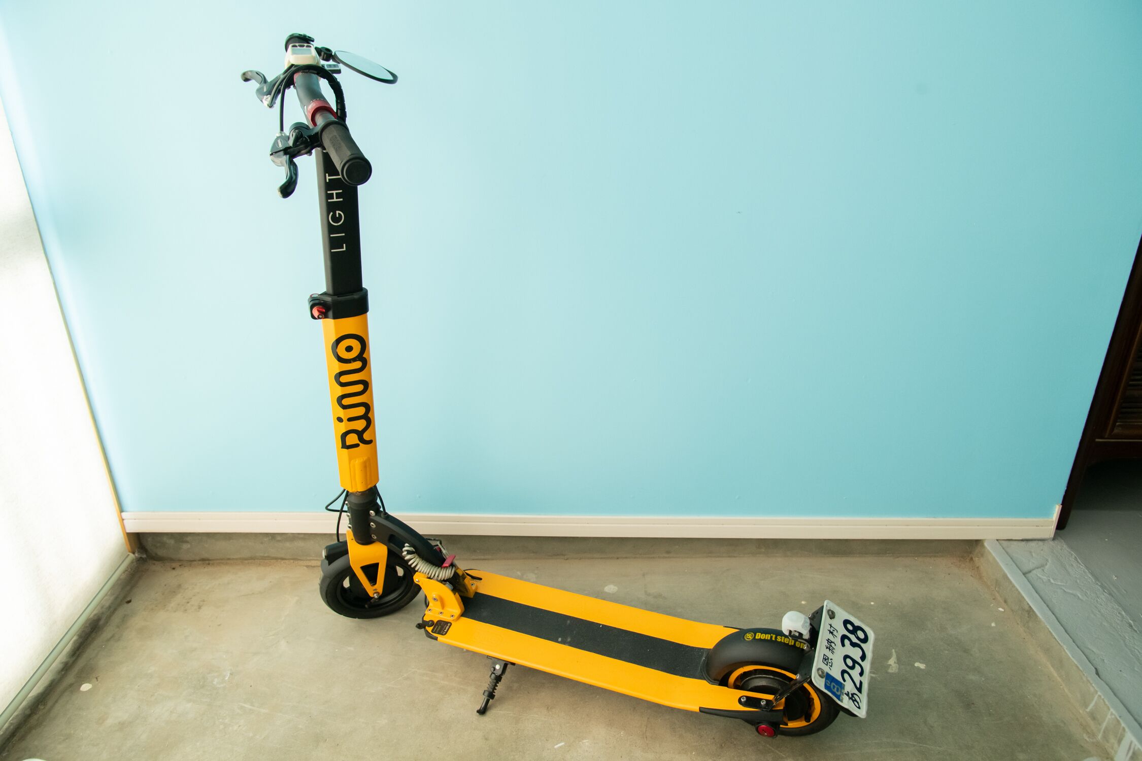 A yellow electric scooter with a license plate, parked indoors against a blue wall.