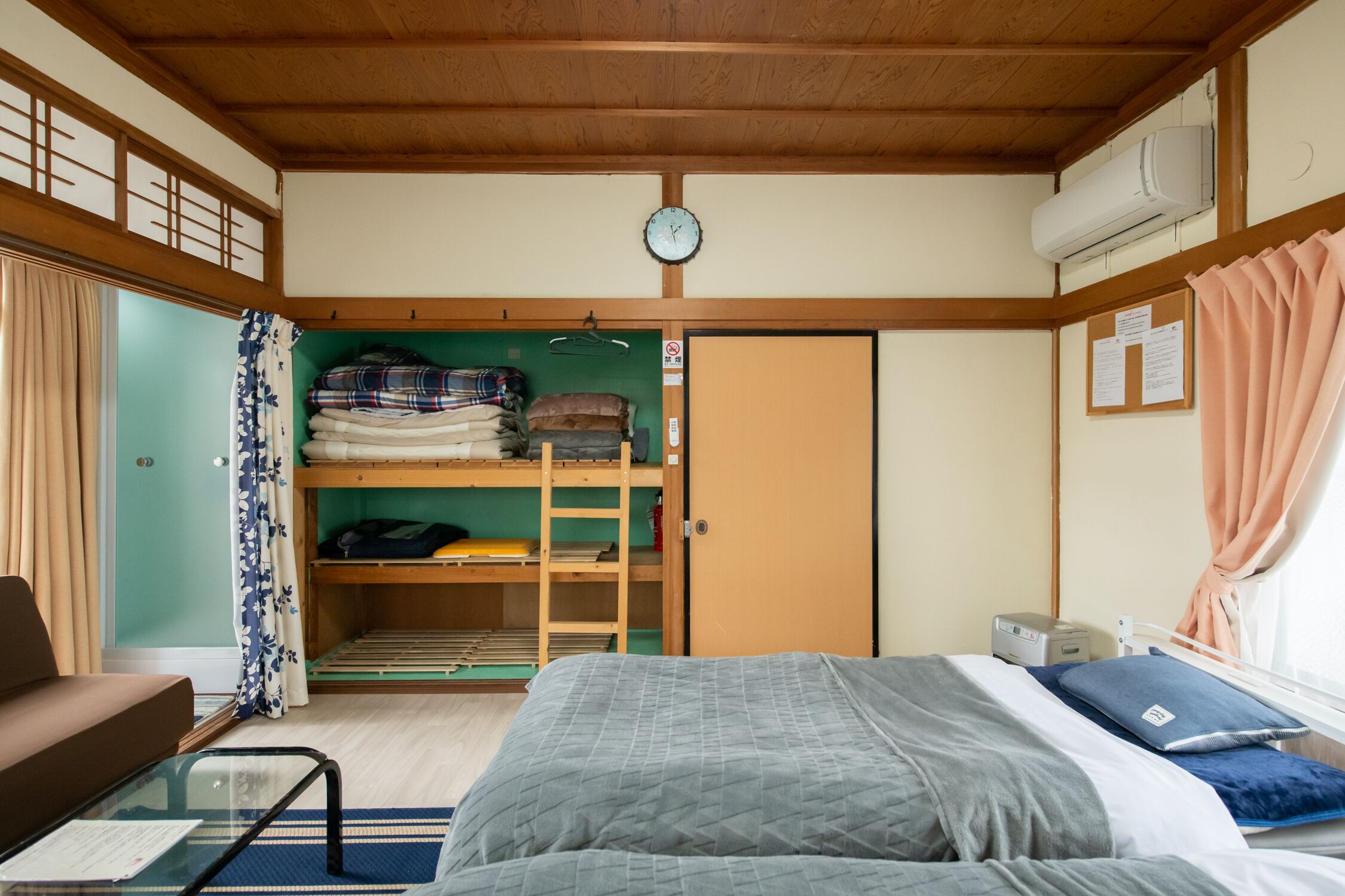Une petite pièce comprenant un lit superposé, une petite table, un canapé et un lit avec un oreiller bleu.