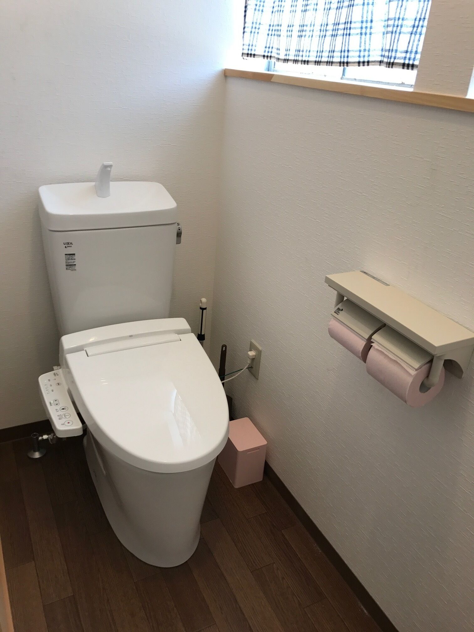 Un baño pequeño y limpio con inodoro blanco, un cubo de basura rosa y un dispensador de papel higiénico en la pared.