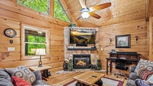A cozy log cabin interior with a stone fireplace, a television mounted above it, and a ceiling fan. - Twilight Point Pet Friendly! Book NOW and receive tickets to Dollywood, Anakeesta and many more (Gatlinburg)