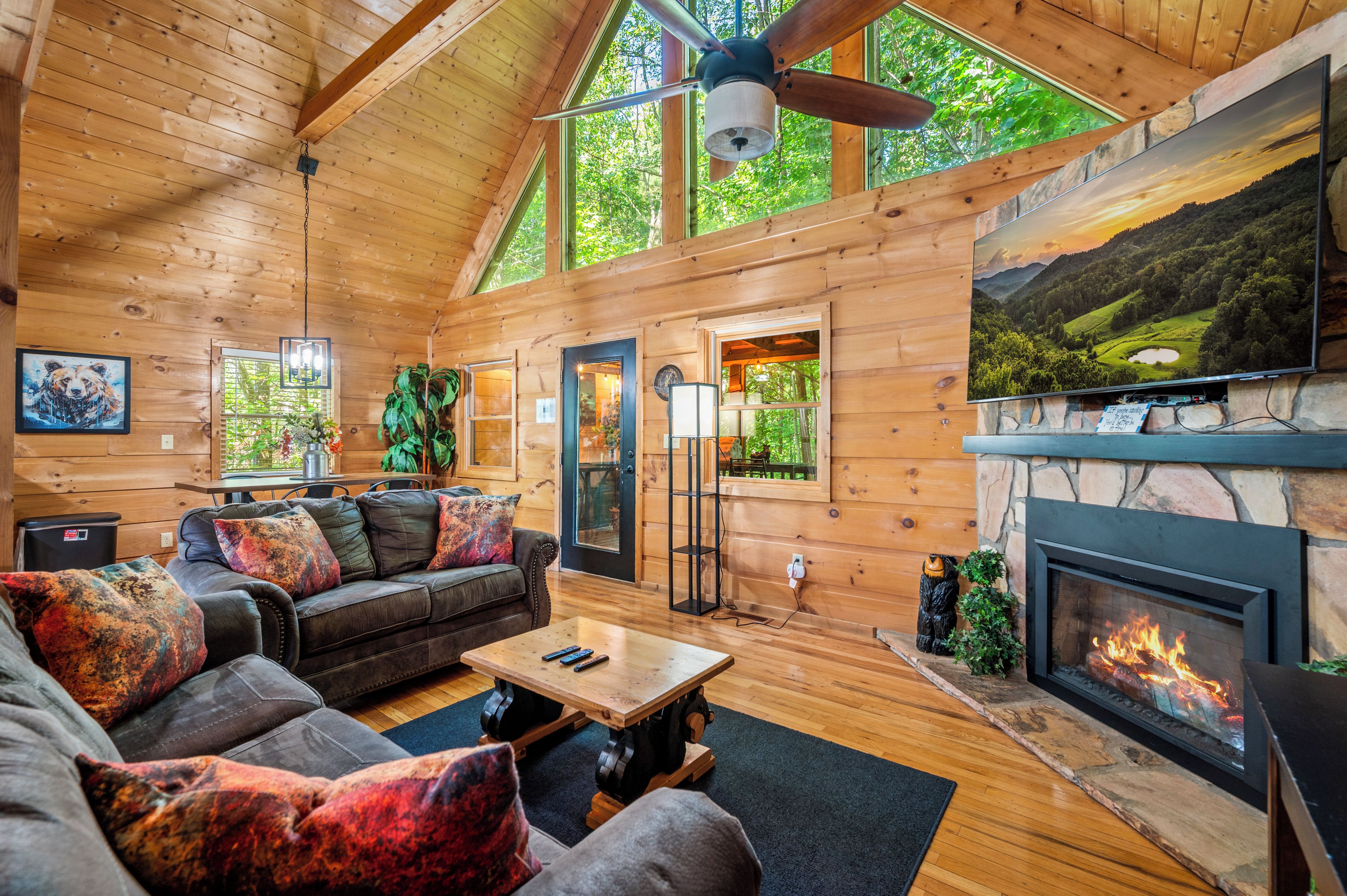 A cozy log cabin interior with a fireplace, wooden furniture, and large windows.