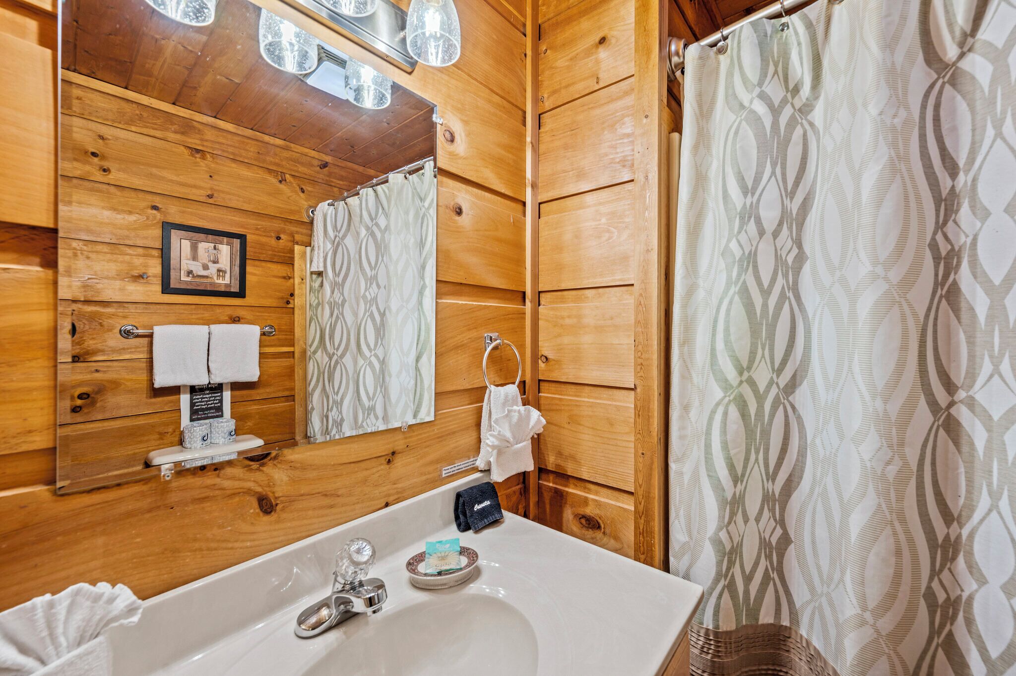 A wooden cabin bathroom with a sink, mirror, towel rack, and patterned shower curtain.