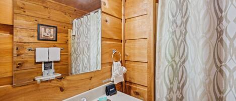 A wooden cabin bathroom with a sink, mirror, towel rack, and patterned shower curtain.