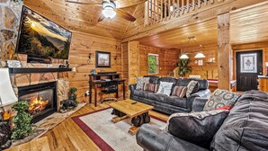 A cozy log cabin interior with a fireplace, leather sofa, wooden coffee table, and a television mounted on the wall. - Twilight Point Pet Friendly! Book NOW and receive tickets to Dollywood, Anakeesta and many more (Gatlinburg)