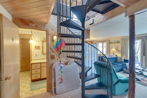 Un intérieur à plusieurs niveaux avec un escalier en colimaçon, un espace de vie avec un canapé et un coin cuisine.