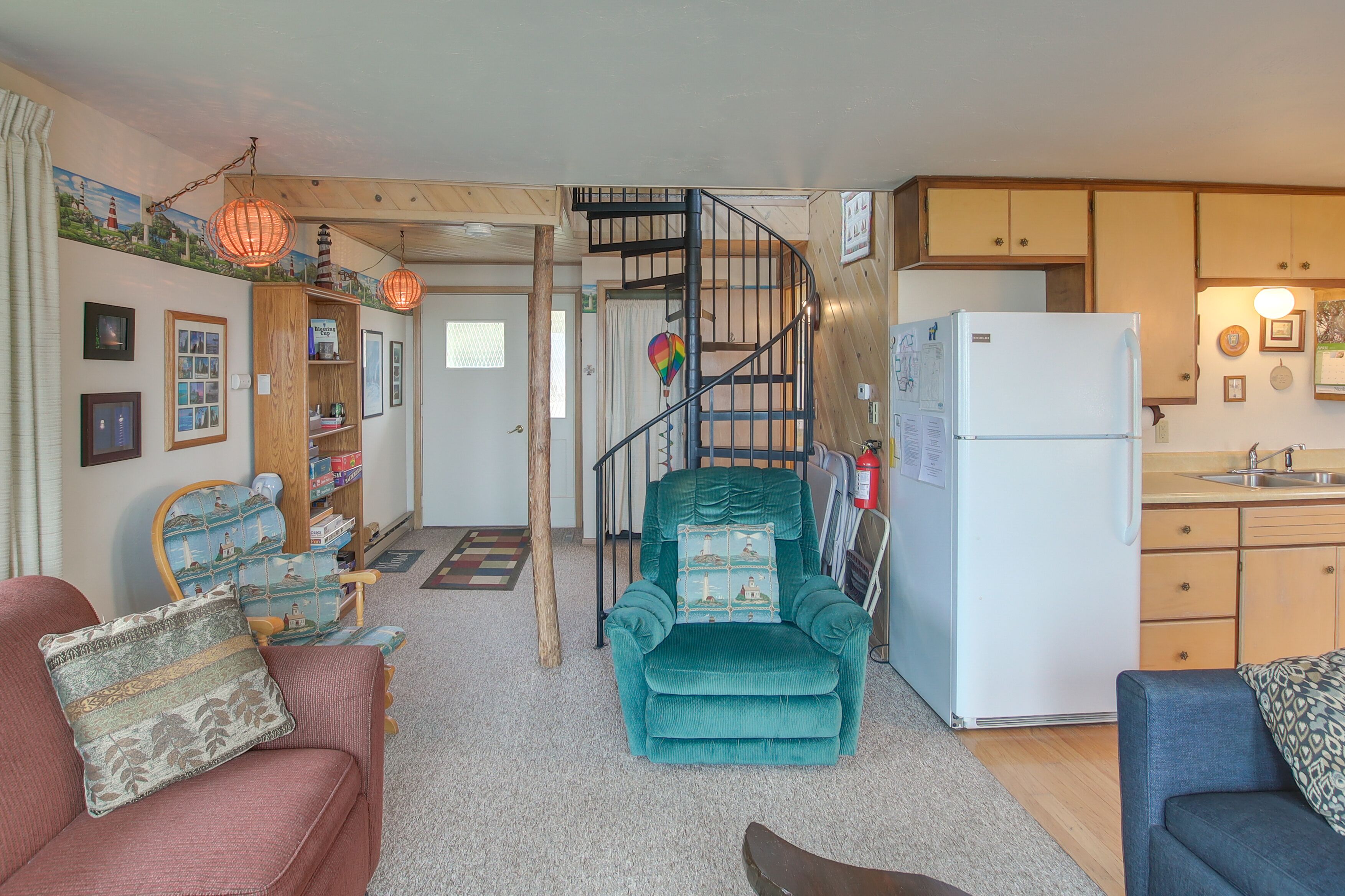Een ruimtelijk ingerichte leefruimte met een trap naar een slaapzolder, een kitchenette en een zithoek met een bank en fauteuil.