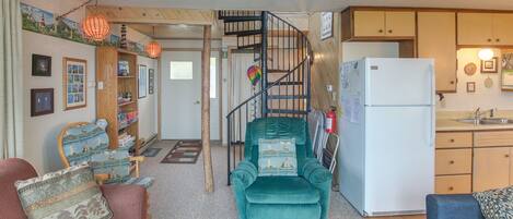 A compact living space with a staircase leading to a loft area, a kitchenette, and a seating area with a sofa and armchair.