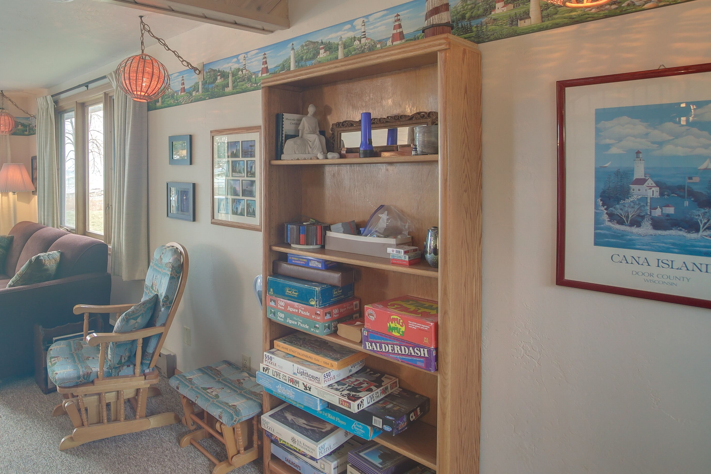 A cozy room with a wooden rocking chair, a bookshelf filled with board games, and a framed picture of a lighthouse.