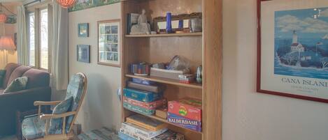A cozy room with a wooden rocking chair, a bookshelf filled with board games, and a framed picture of a lighthouse.