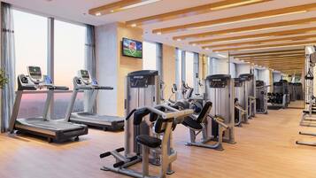 Une salle de sport moderne équipée de tapis de course, de vélos elliptiques et de matériel de musculation.