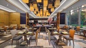 A modern restaurant with a central bar, multiple seating areas, and large windows offering a view of the outdoors. - Nanchang Wanda Realm Hotel (Nanchang)